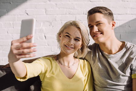 微笑的情侣在家用智能手机自拍图片