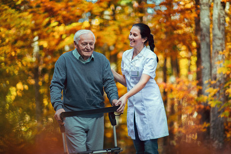 在秋季公园帮助老年男子的年轻护士老年人在户外用助老图片