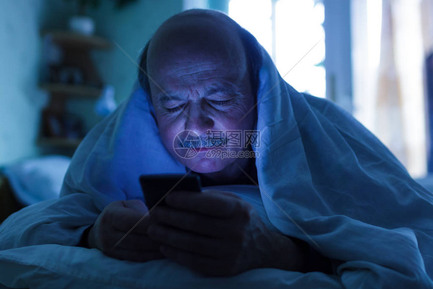 一位老人试图入睡并检查电话中的邮件或电话上网成瘾图片