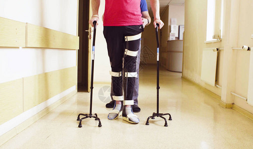 在康复诊所用两根拐杖支撑行走矫形器的残疾人的腿背景图片
