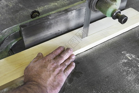 木匠在车间用带锯切割一块木头图片