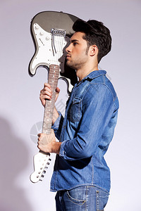 一位年轻吉他手的侧面景象带着灰色背图片