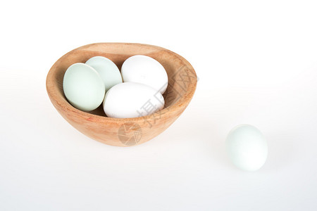 白色桌子上木碗里的绿色和白色鸡蛋图片