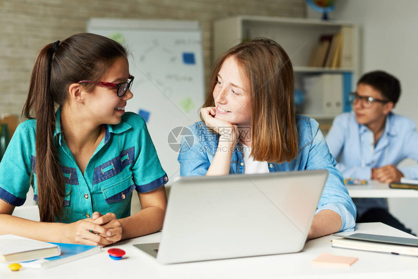 两个十几岁的女孩在学校课间休息时愉快地聊天的图片