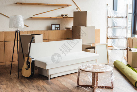 搬迁期间新公寓内的纸板箱滚地毯吉他和家具背景图片