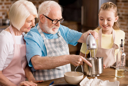 快乐的小女孩和祖父母混合面粉在厨房图片