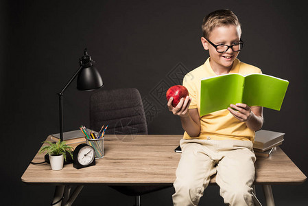 带着苹果做作业的微笑男学生坐在桌子上图片