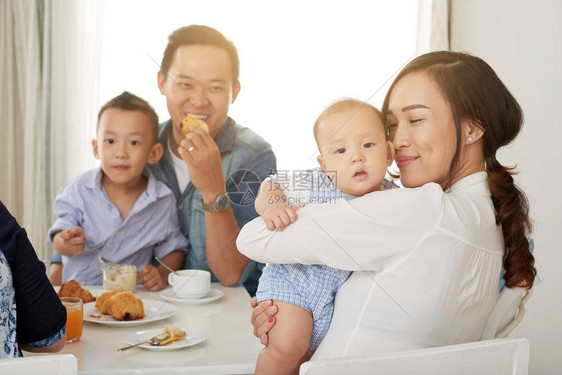 清晨和家人在早餐桌前拥抱可爱小男孩的快乐亚洲女人在阳图片