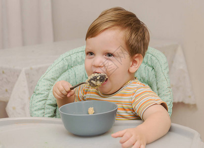 穿条纹T恤衫的金发小金发男孩用灰色盘子上的勺子吃粥背景图片