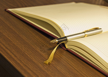 木桌上的钢笔和日记的特写图片