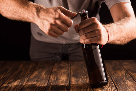 男人在木制桌子上开瓶器打开啤酒背景图片