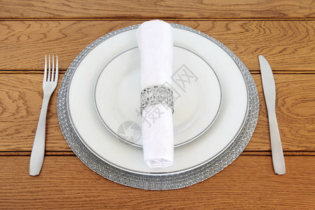优雅的餐桌布置有银色磨碎的瓷板不锈钢餐具单纸巾和在橡树桌背景的图片
