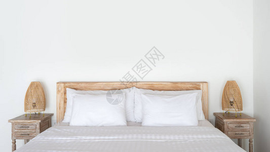 在舒适的卧室里用白色床单枕头在墙壁附近的床边桌子上用夜灯和现代住宅内部复制空间背景图片
