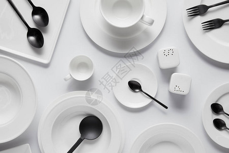 黑汤匙叉子沙拉勺不同盘子碗盐窖胡椒铸机和白桌上的杯图片