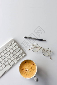 在白桌背景上用键盘钢笔眼镜和热咖啡杯对办公桌工作空间的顶部视图图片