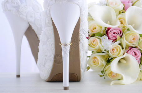 结婚日概念与戒指相伴的脚跟美丽的白色花岗的新娘短裙鞋和花束在白图片