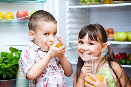 快乐的儿童在冰箱附近喝橙子汁水果蔬菜图片