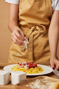 穿着围裙的女人把磨碎的奶酪洒到盘子里的意大利面上的镜头图片