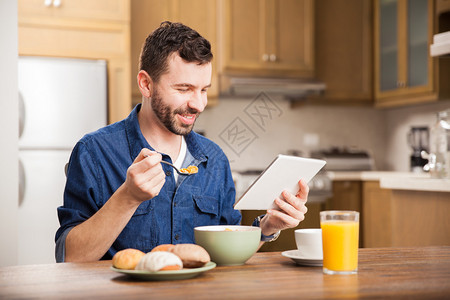 一个留着胡子的男人在家里享用美味早餐时在平板电脑上看电图片