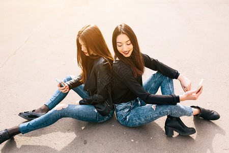 两个年轻成年女坐在外边看一些智能手机里的东西图片