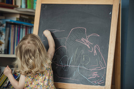 一个小女孩在黑板上画和写字的后视图小女孩伸手在黑板上用不同颜图片