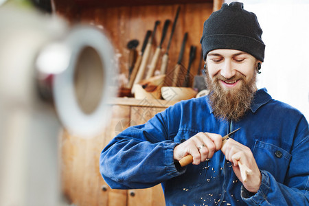 长胡子的工人穿着蓝色牛仔裤西装和黑帽雕刻木头图片