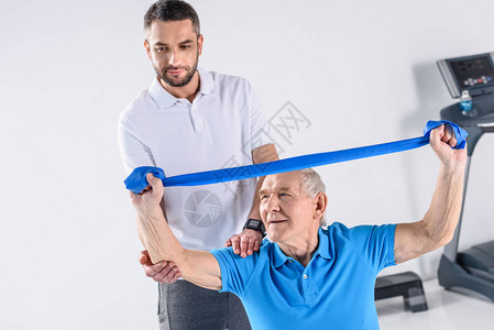协助老年男子使用橡胶带进行锻炼图片