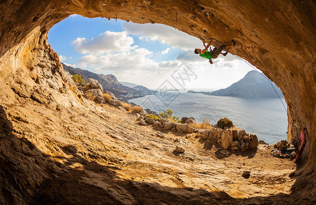 雄登山者爬上悬着的岩石与下面美丽的图片