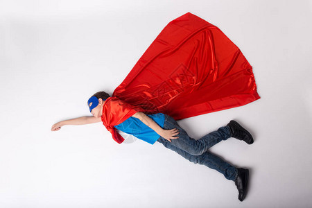 穿着超人服装飞行的超级英雄孩子红色斗篷和蓝色面图片