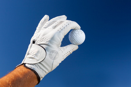 戴高尔夫手套的手拿着白高尔夫球在图片