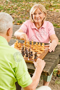 快乐的老年夫妇在公园长椅上下棋图片素材