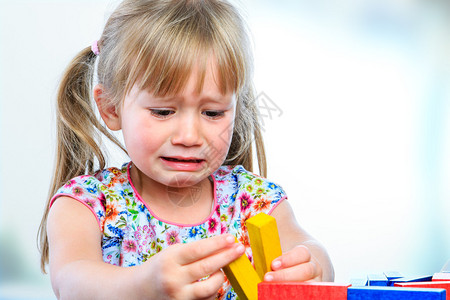 关闭了哭泣的小女孩在餐桌上玩木块的肖像沮丧的女孩表现出喜怒无常图片