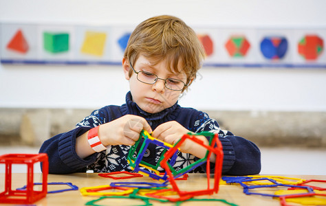 戴眼镜的小孩在数学博物馆里玩很多五颜六色的塑料积木套件小男孩在构建和创建几何图背景图片
