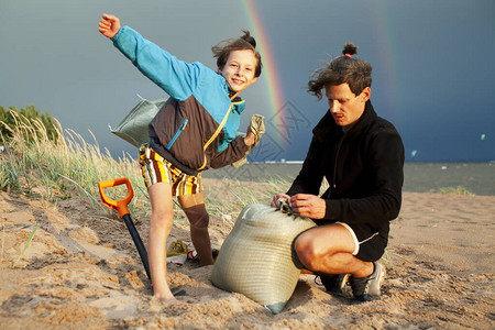 年轻的父亲带着儿子在海滩上在彩虹下挖坑背景图片