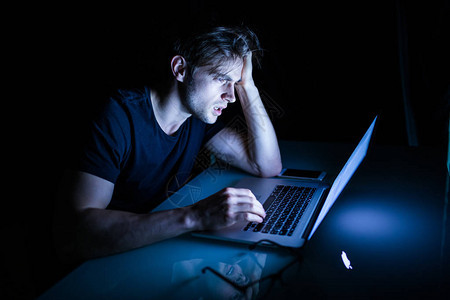 夜里坐在笔记本电脑前的年轻男子感到疲惫图片