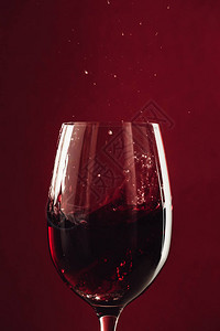 关闭在红色隔离的玻璃杯中的红酒飞溅背景图片