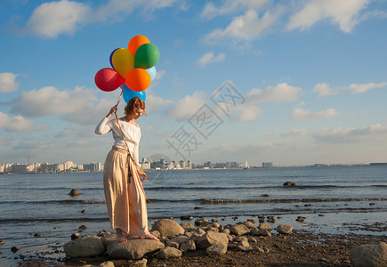 天空气球海湾岩石上拿着五颜六色气球的女孩背景