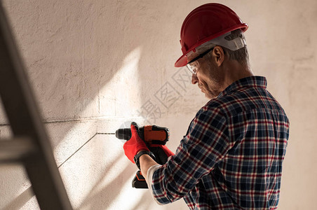 建筑工人用电钻在墙上打洞瓦工在建筑工地的墙上钻孔戴安全帽的成熟男人在墙上打洞图片