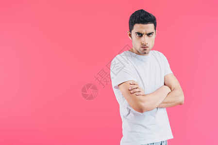 愤怒的英俊帅哥站着双臂交叉看着被粉红色背景图片