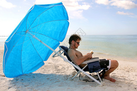 一个年轻人坐在海滩伞下面向大海看书图片
