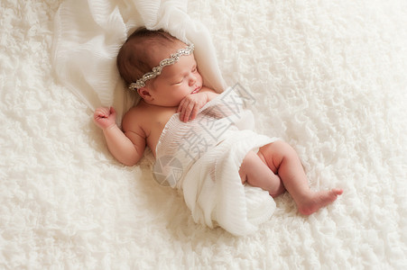 一个戴着水钻头带的睡觉8天大的新生女婴的俯视图她裹着白色的薄纱背景图片