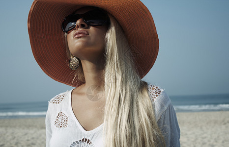 在沙滩上美丽的金发美女戴着沙滩帽和墨镜看着天空图片