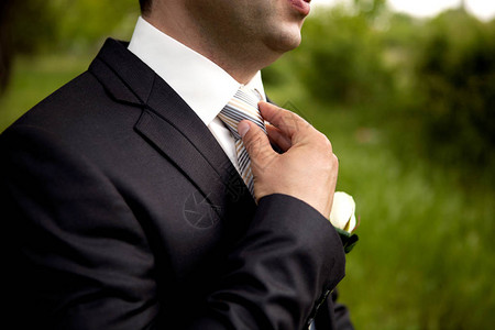穿西装的新郎用手纠正领带特写构图图片