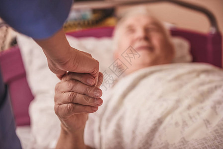 老人在躺医院病房的床上看着护士握着她的手和微笑图片