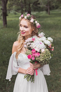 戴着花环的美丽微笑的年轻新娘拿着婚礼花图片