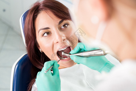 对办公室的女病人进行牙科钻修复牙齿的牙医图片