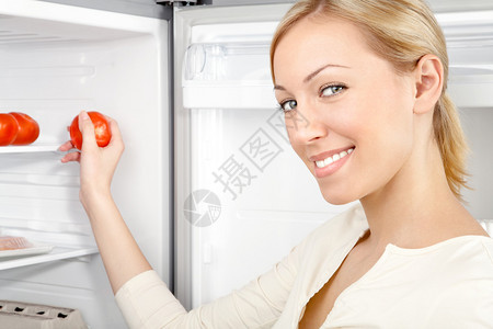 微笑的女人从冰箱里拿出一个西红柿图片