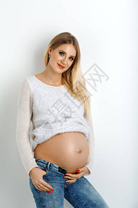 穿牛仔裤和白毛衣的漂亮怀孕年轻女子图片
