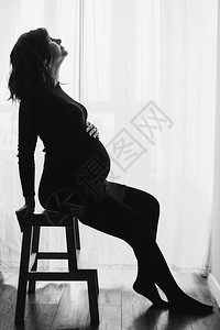 穿着时尚黑色连衣裙的快乐孕妇的剪影坐在梯子上图片