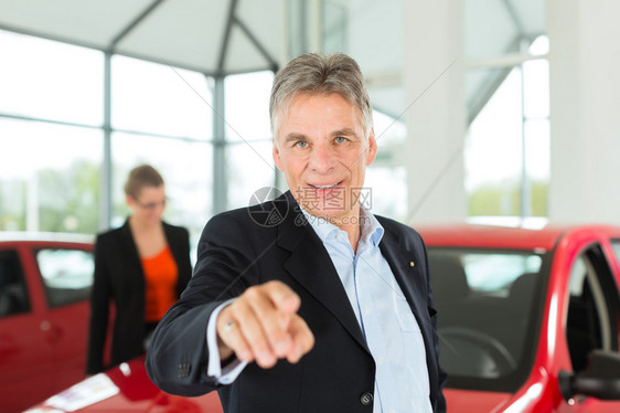 成熟的单身男子在轻型汽车经销店与一位女顾客一位年轻女他显然是在买车或图片